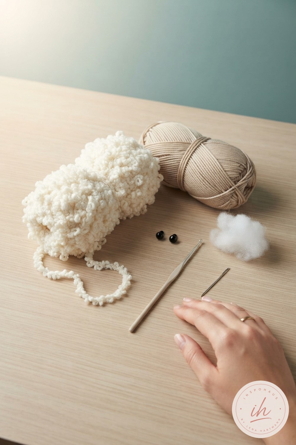 Materialien zum Lamm Amigurumi häkeln: Bouclégarn, Baumwollgarn, Häkelnadel und Sicherheitsaugen liegen auf Holztisch bereit
