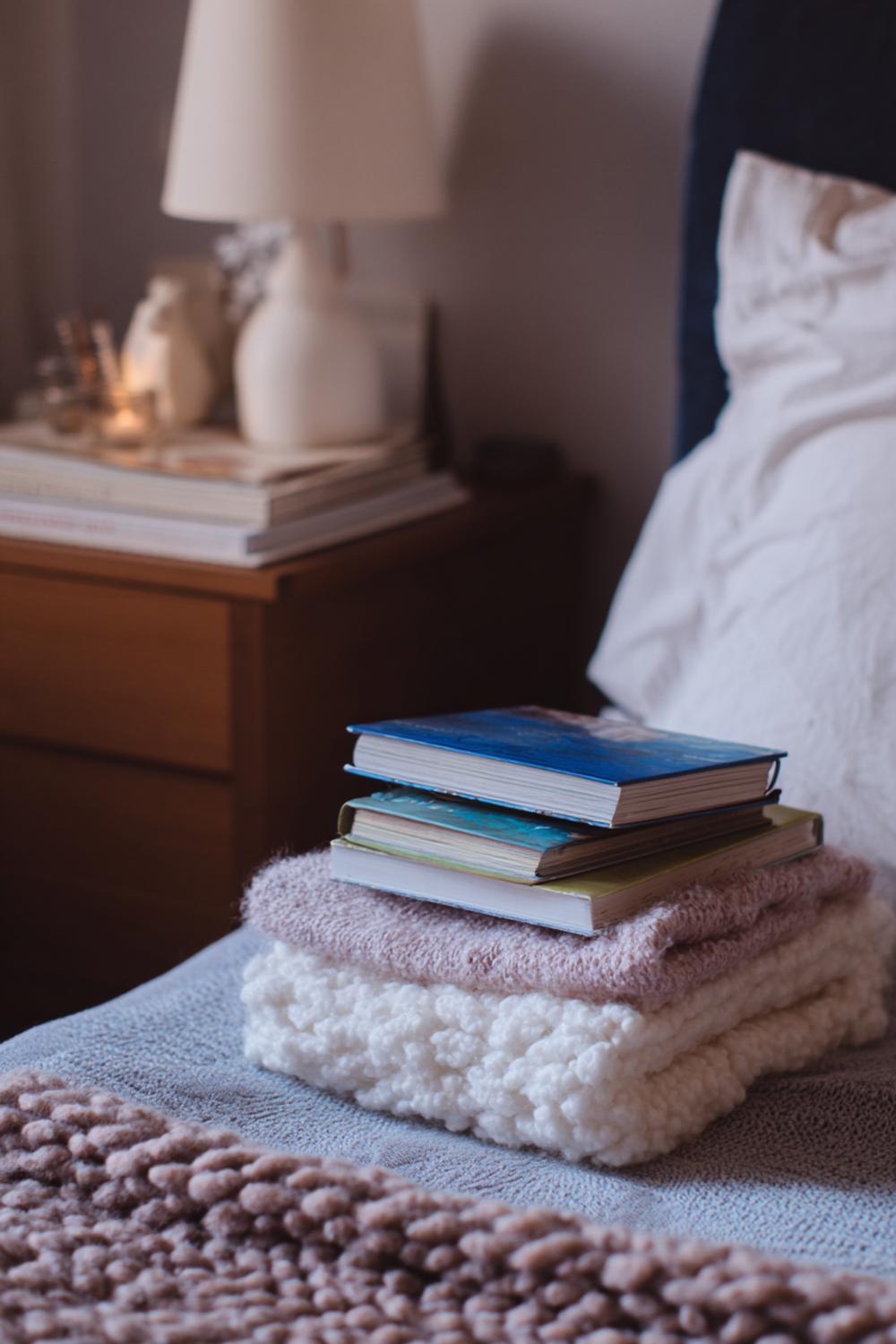 23. Nachttisch-Dekoration mit Bücherstapel, Strickdecke und sanften Neutraltönen