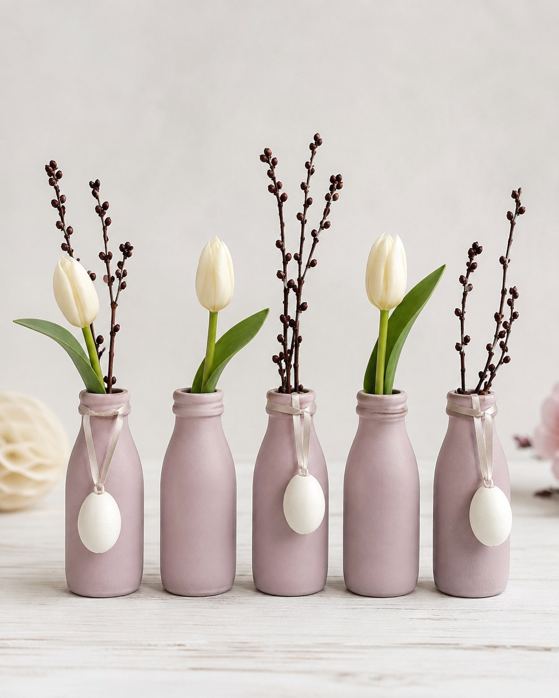 Zart rosa bemalte Fläschchen mit Tulpen und Kätzchenzweigen als österliche Tischdeko.