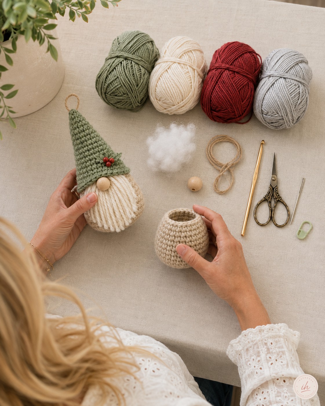 Flatlay mit Garnknäueln in Sage, Creme, Rot und Hellgrau vor dem Weihnachtsgnome häkeln auf Leinentisch